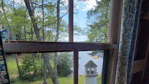 A window with a view of a grassy area, a tree, and a small white structure. - "Uptacamp" feel, true Maine style Camp (Lincolnville)