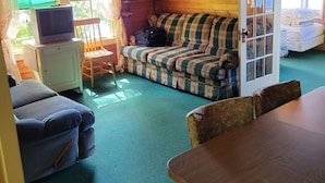 A cozy cabin interior with a plaid sofa, a wooden dining table, a television on a cabinet, and a window with curtains. - "Uptacamp" feel, true Maine style Camp (Lincolnville)