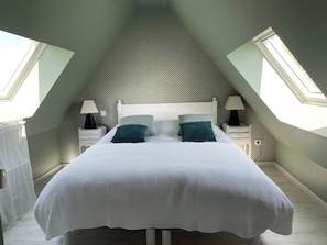 A bedroom with a sloped ceiling, a bed with white bedding, two nightstands with lamps, and a window on one side. - Charming and stylish vacation homes (Tardinghen)