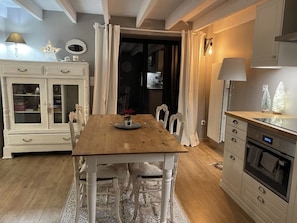 Un'area pranzo con tavolo in legno, sedie bianche, un mobile con vetrine e una cucina con piano cottura.