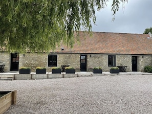 A stone building with a tiled roof, multiple black-framed windows, and outdoor seating areas with black chairs and tables. - Charming and stylish vacation homes (Tardinghen)