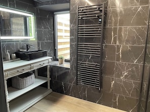 Un bagno con una parete in marmo nero, un mobile lavabo bianco con uno specchio, un porta asciugamani nero e una piccola finestra con vista su un edificio.