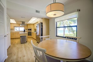 Una cocina moderna con armarios de madera, un refrigerador de acero inoxidable y un comedor con una mesa redonda y sillas blancas.