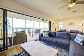 A spacious living area with a large sofa, a coffee table, and a balcony with a view of the ocean.