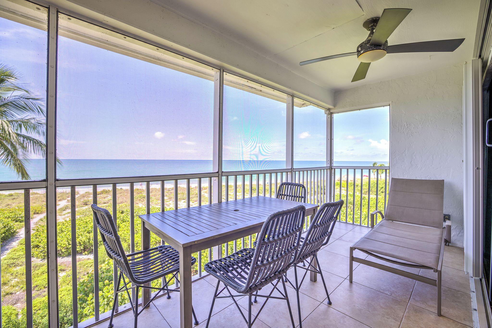 Un balcon avec une table et des chaises, un ventilateur de plafond et une vue sur l’océan.