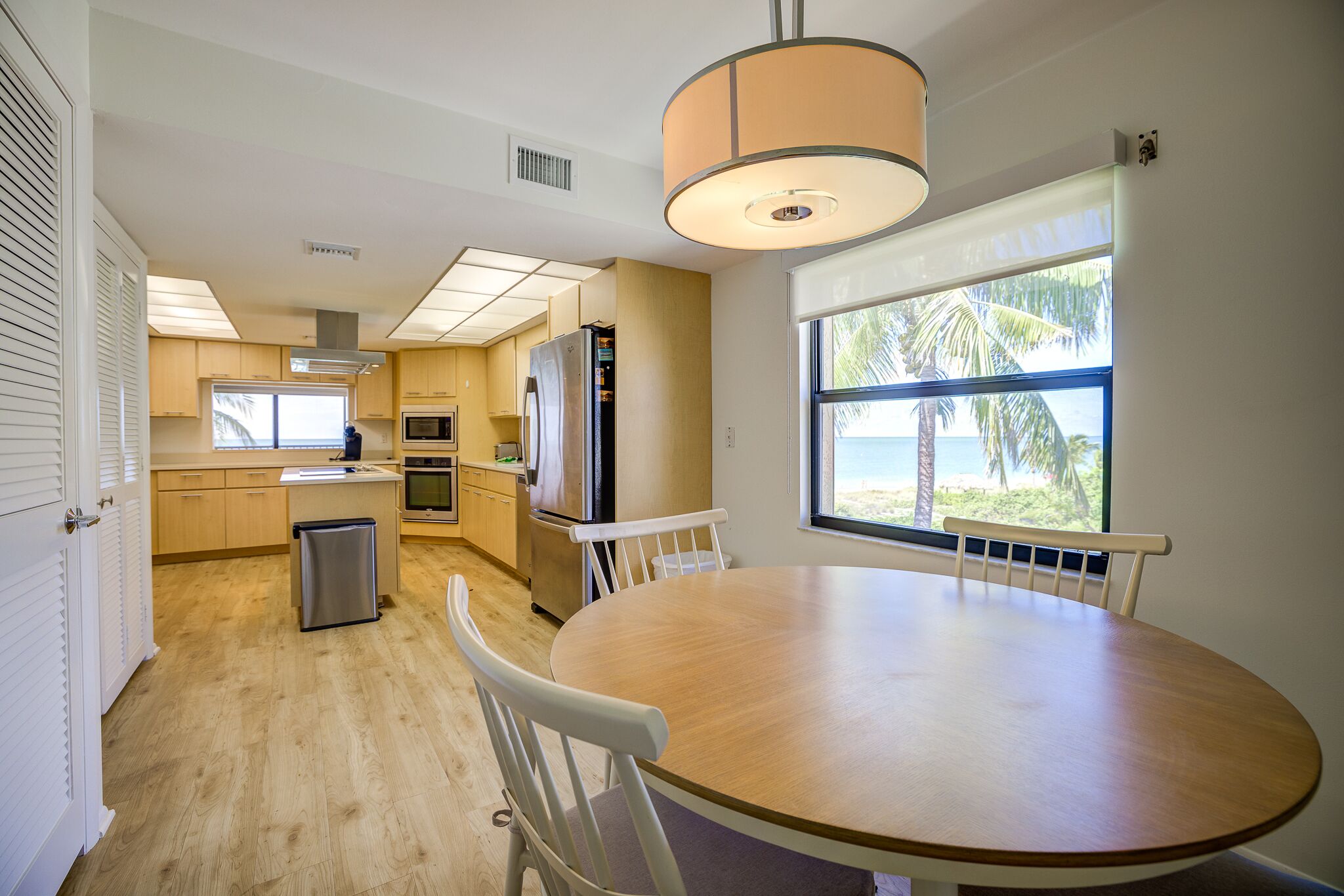 A modern kitchen with wooden cabinets, a stainless steel refrigerator, and a dining area with a round table and white chairs.