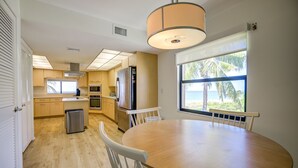Una cocina moderna con armarios de madera, un refrigerador de acero inoxidable y un comedor con una mesa redonda y sillas blancas.