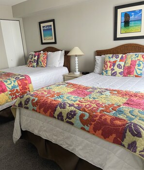 A hotel room with two beds, colorful floral bedding, a lamp, and framed pictures on the wall. - Beachfront Escape to Unwind & Take in the Ocean Air (Myrtle Beach)