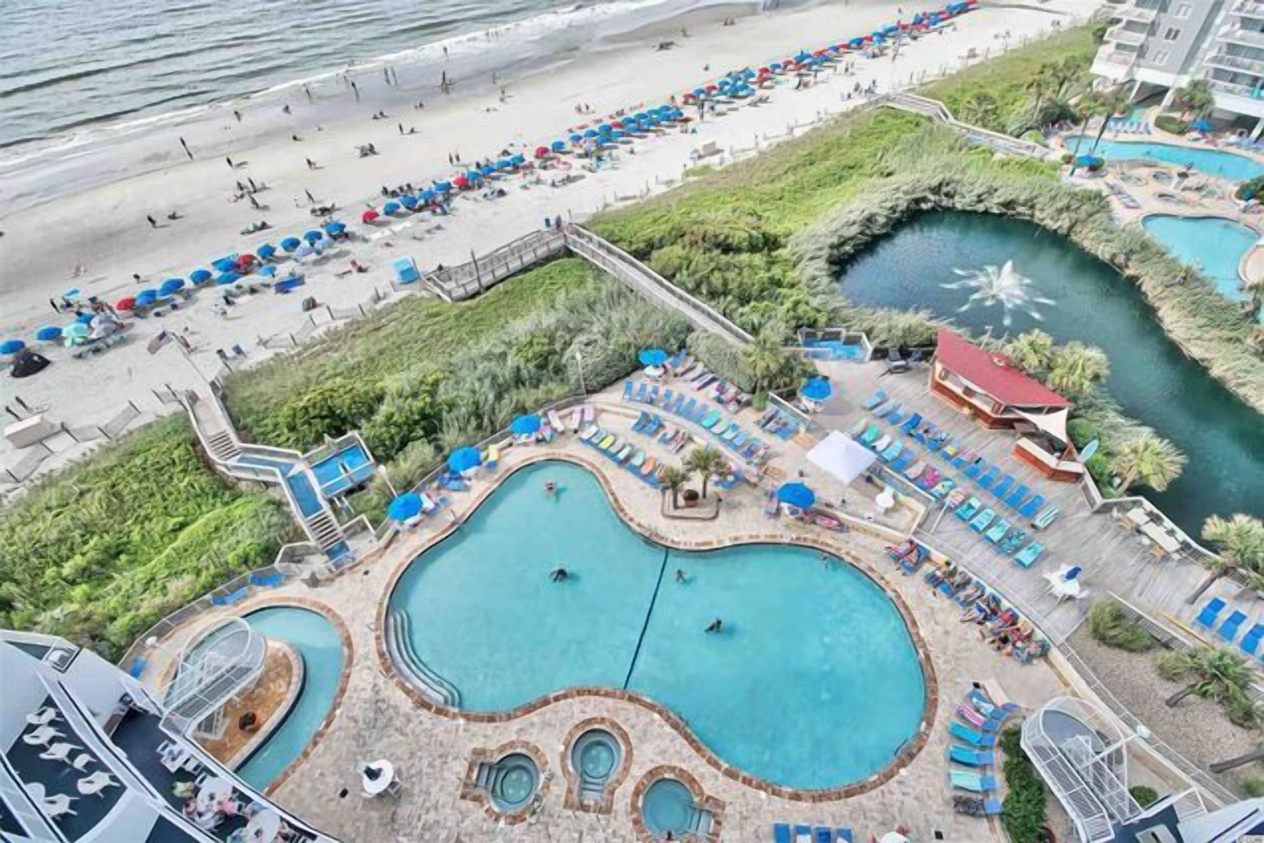 An aerial view of a resort with multiple swimming pools, a beach area, and a landscaped garden.