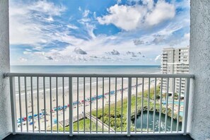 A balcony with a view of a beach, a pool, and a building in the background. - Beachfront Escape to Unwind & Take in the Ocean Air (Myrtle Beach)