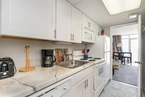 A compact kitchen with white cabinets, a microwave, a coffee maker, and a sink. - Beachfront Escape to Unwind & Take in the Ocean Air (Myrtle Beach)