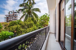 A balcony with a metal railing, a view of a multi-story building, and lush greenery.