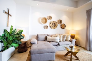 A modern living room with a grey sofa, a glass coffee table, and decorative woven plates on the wall. - Pool, 2 Balconies, Romantic Zone, Walk Everywhere (Puerto Vallarta)