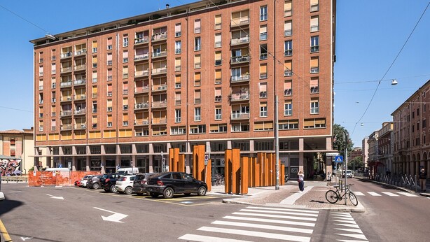 Un edificio residencial de varios pisos con balcones, un paso de peatones y automóviles estacionados.