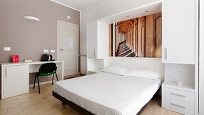 Ein Hotelzimmer mit Bett, Schreibtisch mit Stuhl, Heizkörper und einem Wandbild.