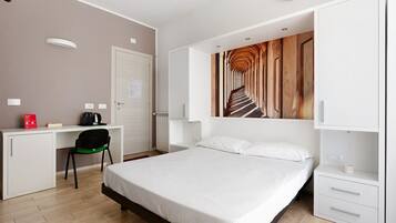 Een hotelkamer met een bed, een bureau met een stoel, een radiator en een kunstwerk aan de muur.
