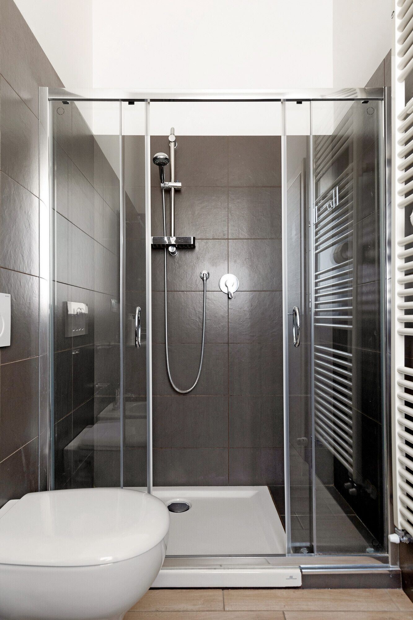 Een moderne badkamer met een douchecabine van glas, een wit toilet en een ingebouwde handdoekhouder.