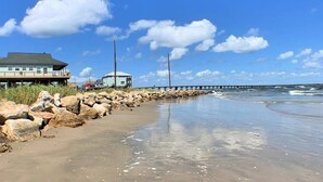 Une plage bordée d’une digue rocheuse, une jetée s’avançant dans l’eau et un bâtiment doté d’un balcon donnant sur la plage.