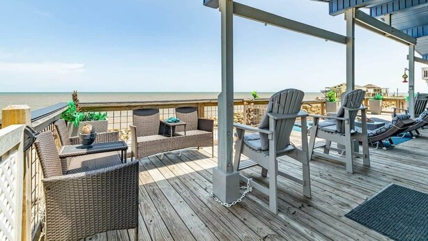 Une terrasse extérieure couverte, aménagée avec des meubles en osier, une table et des chaises, et offrant une vue sur la plage.