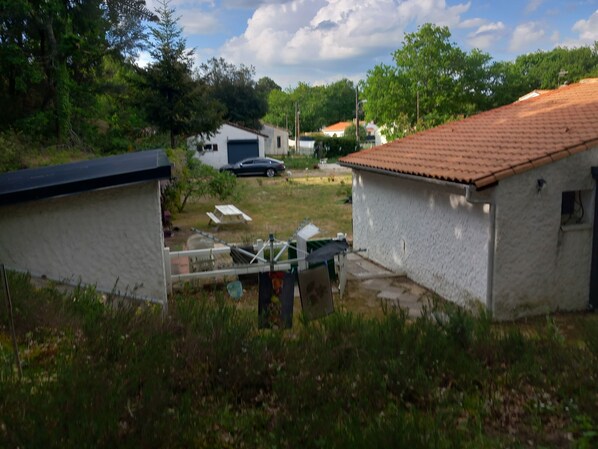 A residential area with two white buildings, one with a red-tiled roof. There is a car parked in the background, and a picnic table is visible in the yard.