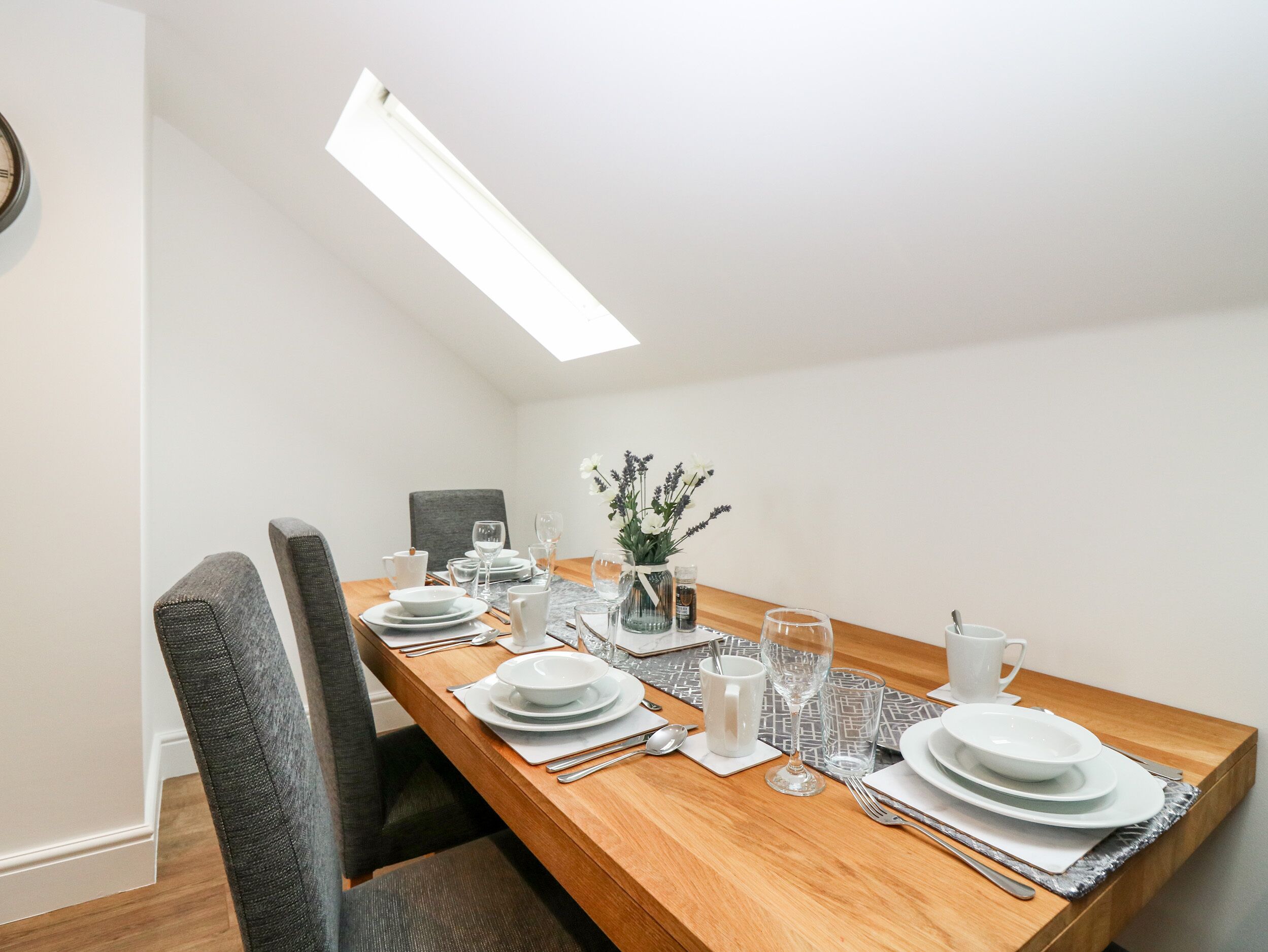 Uma sala de jantar com uma mesa de madeira posta para quatro pessoas, incluindo pratos, copos e talheres.