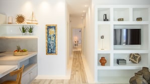A modern kitchen with a dining area, wooden flooring, and a hallway leading to a bedroom.
