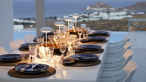 A dining table set with plates, glasses, and cutlery, overlooking a coastal landscape with buildings in the background.