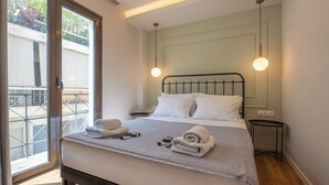 Ein ordentlich bezogenes Bett mit weißen Leinen und Handtüchern, ein kleiner Nachttisch und Blick auf einen Balkon durch eine Glastür.