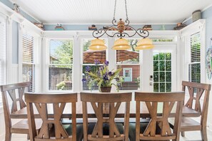 A dining area with a wooden table and chairs, a hanging light fixture, and a view through a window with blinds.