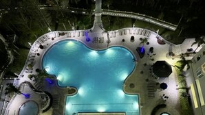 Una piscina grande y de forma inusual, rodeada de zonas de descanso y un puente.