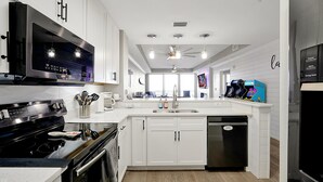 Una cocina moderna con armarios blancos, estufa negra, lavavajillas y ventilador de techo.