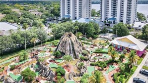 Zona residencial con edificios altos, un parque ajardinado y una formación rocosa, y un pequeño edificio con techo rosa.