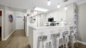 Una cocina moderna con armarios blancos, una isla central con taburetes y un microondas.