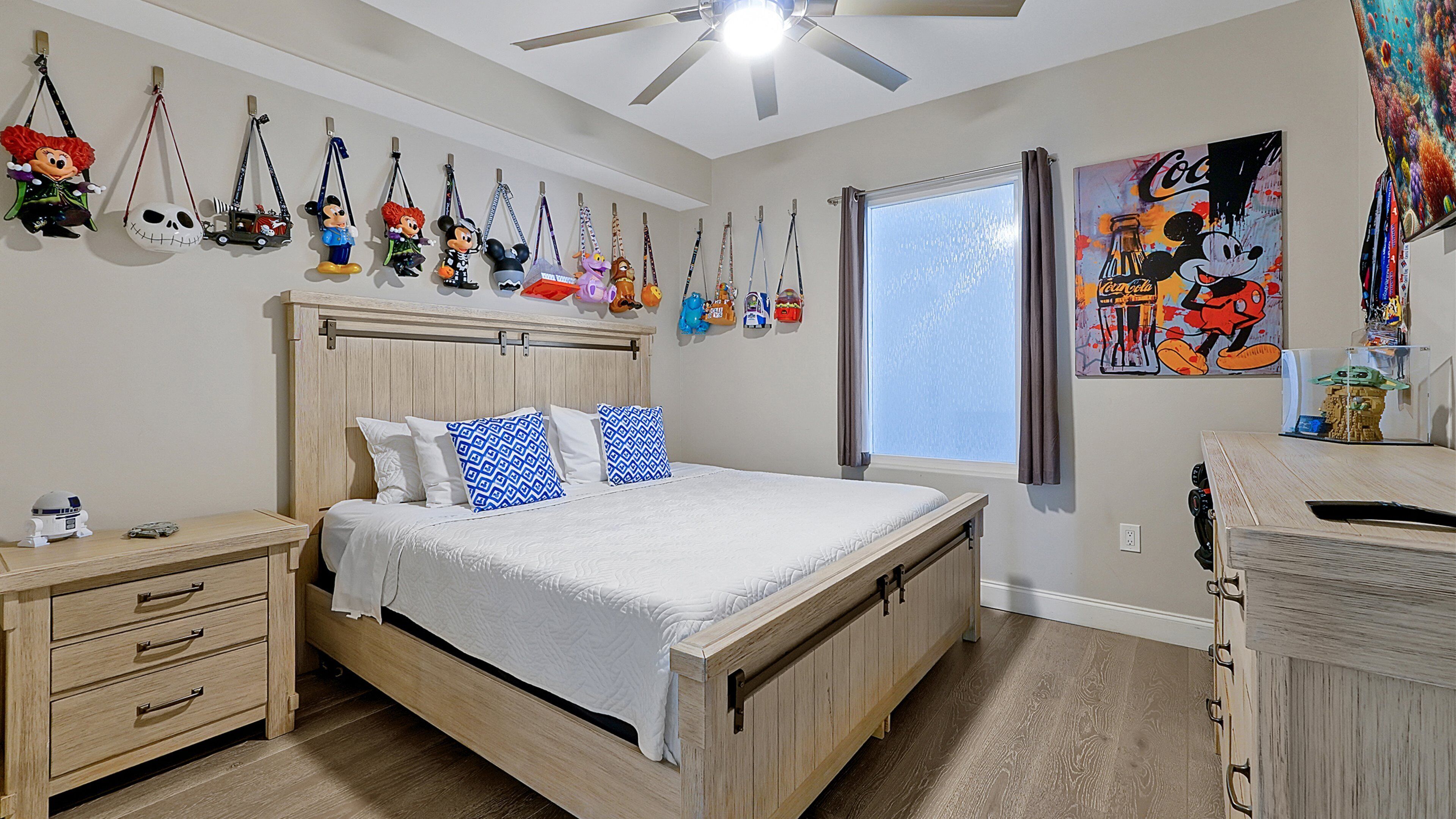 A bedroom with a wooden bed, bedside tables, a ceiling fan, and wall decorations including figurines and a poster.