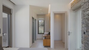 A modern bedroom with a large bed, a bathroom with a vanity, and a stone accent wall. - Impeccable design, total privacy & heated pool with sea views (Rethymno)
