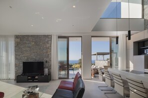 A modern living room with a stone wall, a flat-screen TV, a leather sofa, and a glass coffee table.