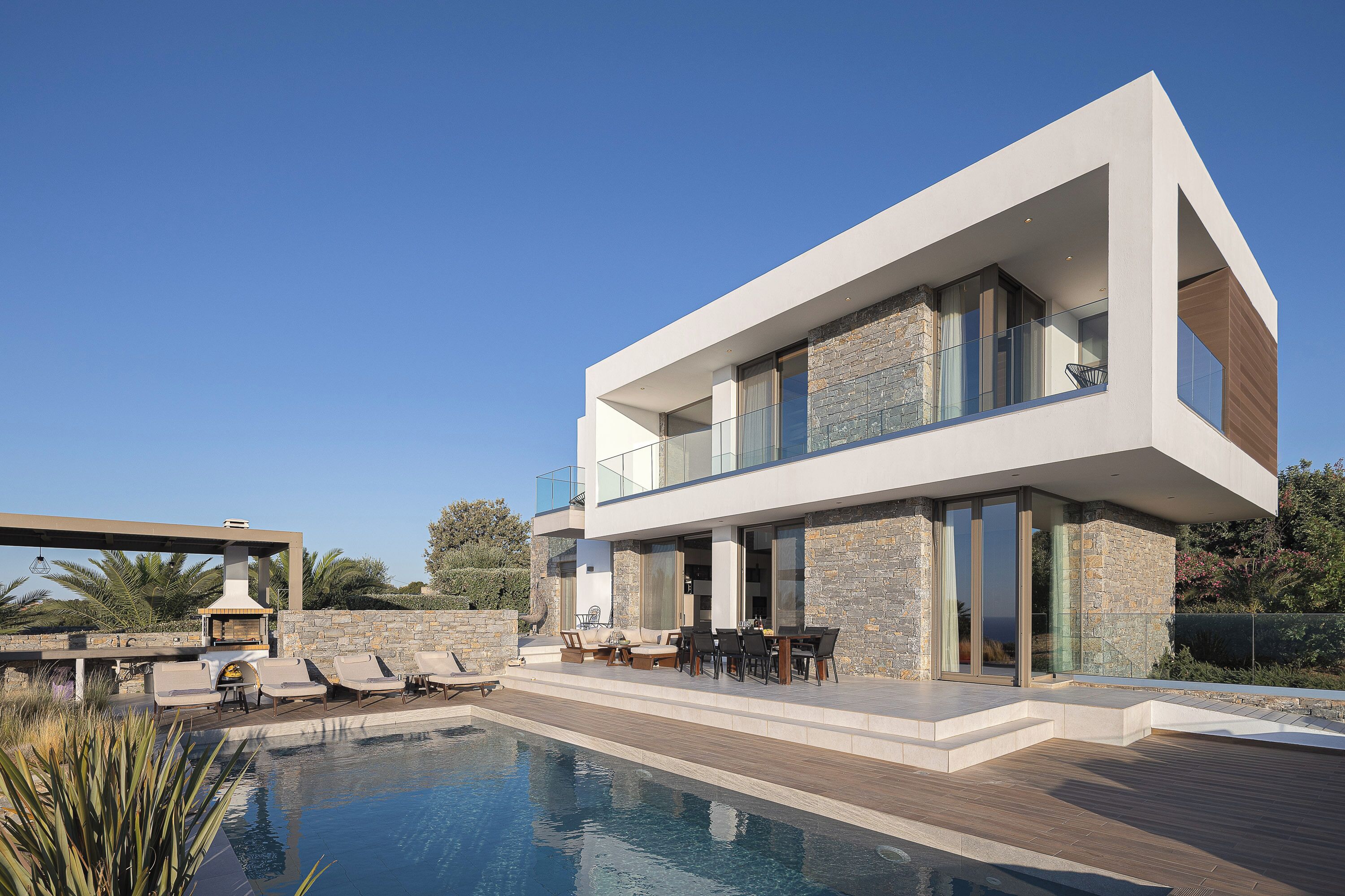 Una casa moderna de dos pisos con piscina, mobiliario exterior y fachada de piedra.