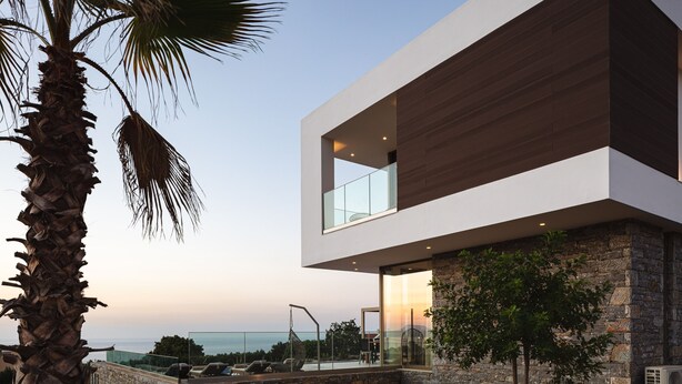 A modern two-story building with a stone facade, large windows, and a view of the sea. - Impeccable design, total privacy & heated pool with sea views (Rethymno)