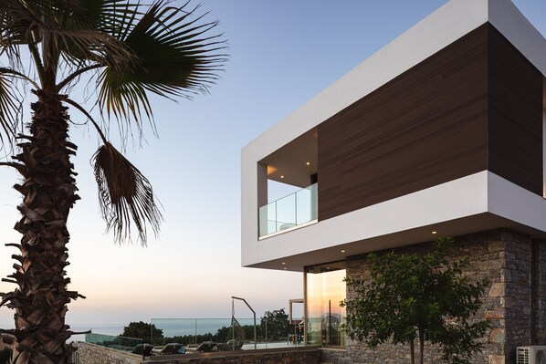 A modern two-story building with a stone facade, large windows, and a view of the sea.