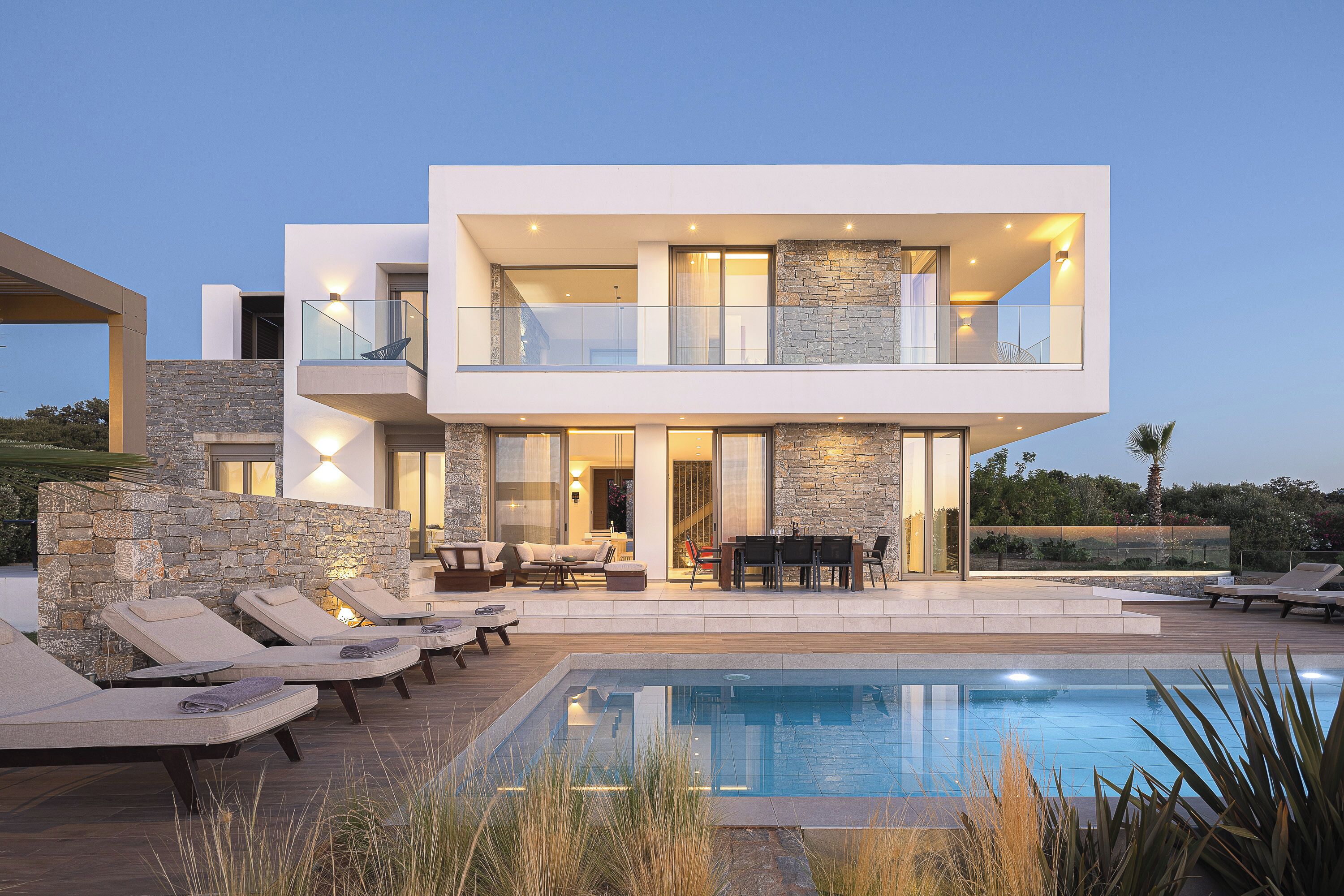 A modern two-story house with a swimming pool, outdoor seating, and a stone facade.