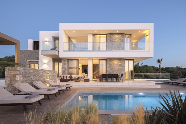 A modern two-story house with a swimming pool, outdoor seating, and a stone facade.