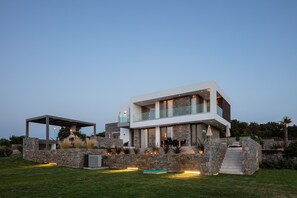 Une maison moderne à deux étages, dotée d’une façade en pierre, d’un patio couvert et d’une piscine.