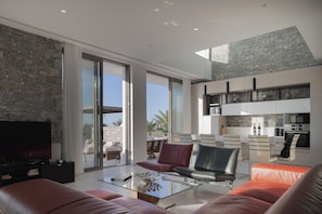 A modern living room with a stone wall, large windows, and a flat-screen TV. - Impeccable design, total privacy & heated pool with sea views (Rethymno)