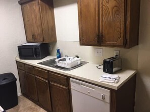 Une cuisine compacte dotée de meubles en bois, d’un four à micro-ondes, d’un grille-pain et d’un lave-vaisselle.