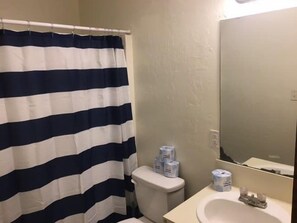 Une salle de bain avec un rideau de douche à rayures, des toilettes, un lavabo avec un miroir et du papier toilette accroché au mur.