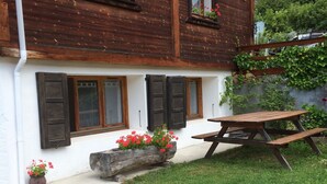 A wooden chalet with three windows, each with a wooden shutter. There is a wooden bench and a picnic table in front. - Charming T3 in a hamlet (Saint-Gervais-les-Bains)