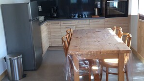 A modern kitchen with a wooden table, built-in appliances, and a ceiling light fixture. - Charming T3 in a hamlet (Saint-Gervais-les-Bains)