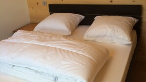 A bed with white bedding and a wooden headboard in a room with a wooden wall. - Charming T3 in a hamlet (Saint-Gervais-les-Bains)