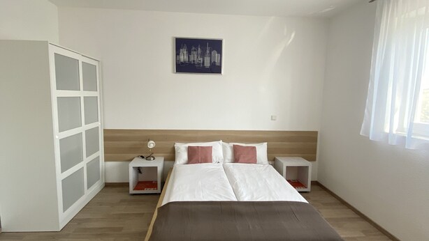 A bedroom with a bed, a nightstand, a wardrobe, and a cityscape artwork on the wall. - MyHome10, Wiesbaden-Mainz, Apartment No: 6 (Wiesbaden)