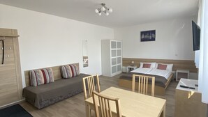A modern, well-lit room with a dining table, chairs, a sofa, a bed, and a TV. - MyHome10, Wiesbaden-Mainz, Apartment No: 6 (Wiesbaden)